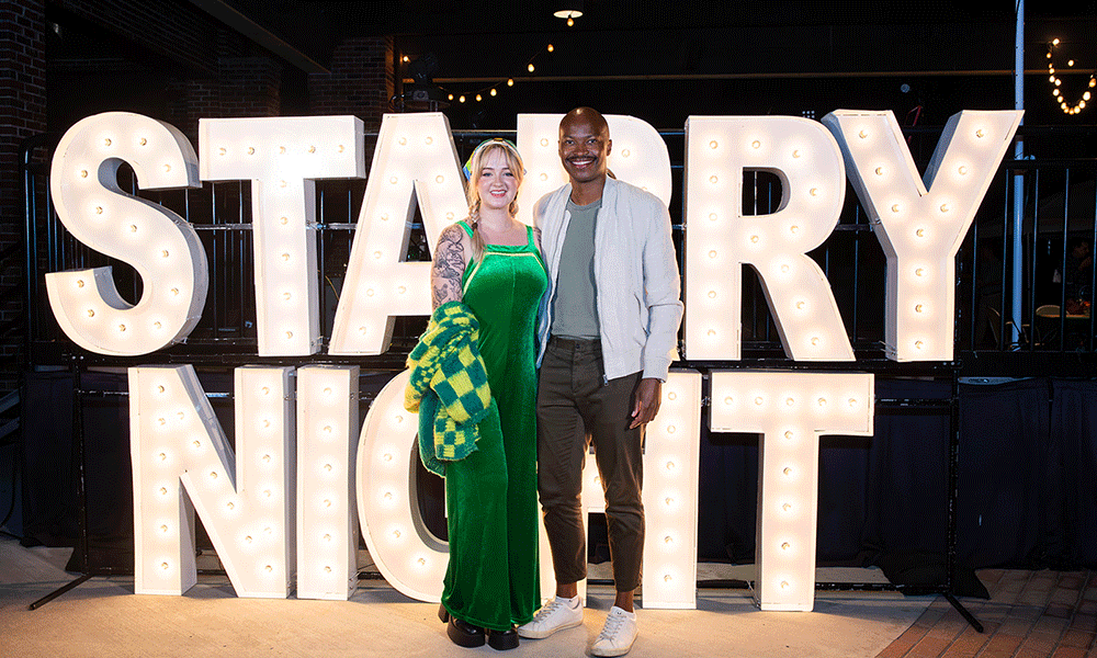 A man and a woman pose in front of a sign for Starry Night.