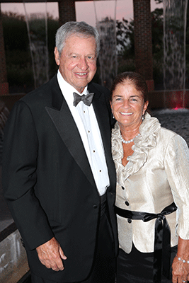 A man with gray hair wearing a tuxedo and a woman with brown hair wearing a formal dress post for the camera.