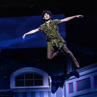 White male wearing green tights and a tunic is flying in midair.