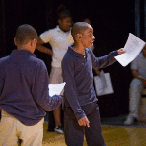 A boy singing during rehearsal while another boy waits to sing with him.