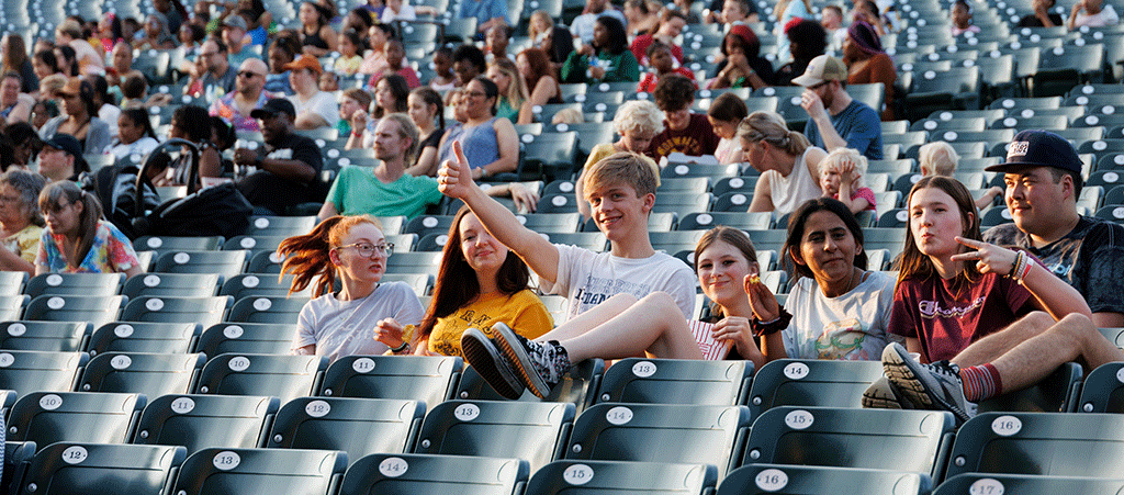 A group of young people sitting in the seats and waving at the camera.