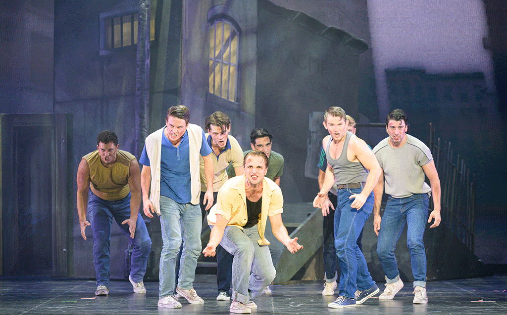 A group of men in the Jets gang dancing on stage during West Side Story.